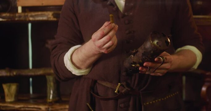 Merchant studies stick and pays attention to guest in shop. Smiling bartender tries to serve customer best in magic potion ingredients store. Medieval trader