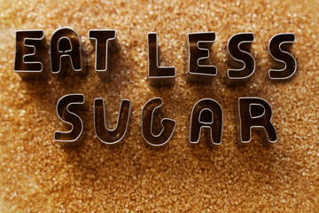 iron words -  EAT LESS SUGAR less made from metal letters on pile of dark Brown cane sugar. sweet...