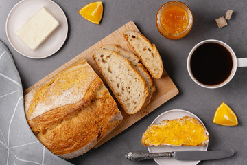Cup of coffee, sandwich with orange jam, loaf of bread on the grey background. Breakfast concept