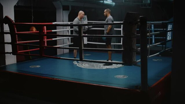 African American fighter in boxing gloves stands on ring and talks with trainer. Caucasian coach explains fighting techniques and consult boxer before competition. Physical activity and workout.
