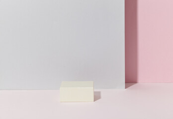 a white square podium against light pink and light grey background. An empty platform for display cosmetic products, food and props.