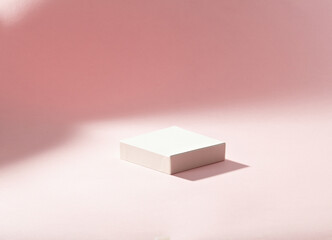 a white square podium against light pink background. An empty platform for display cosmetic products, food and props.