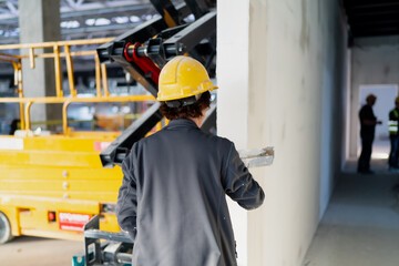 Female construction worker applies plaster on construction project wall with construction lift equipment background