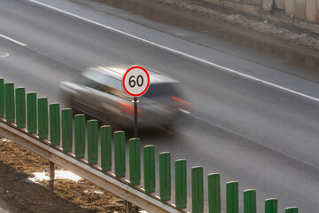 Speed limit 60 sign on city highway with cars speeding in the background