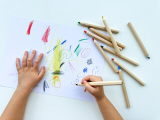 small child draws with colored pencils on paper on white table.