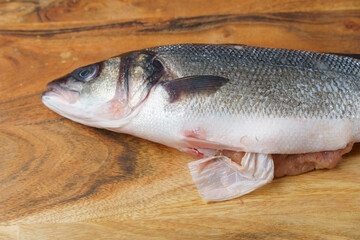 sea bass on a wooden table with a piece of plastic coming out of it, plastic concept in the sea