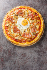 Italian Pizza Bismarck topped with tomato sauce, melted cheese, egg, mushrooms, ham close-up on a wooden board on the table. Vertical top view from above