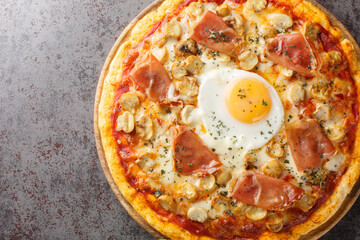 Bismark is the name of a traditional Italian pizza topped with tomato sauce, mozzarella, prosciutto, and egg closeup on the wooden board on the table. Horizontal top view from above