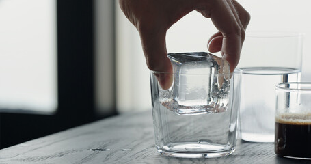 making espresso tonic, add ice cube in tumbler glass and pour espresso on black wood table