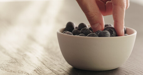 take blueberries from white bowl on oak table
