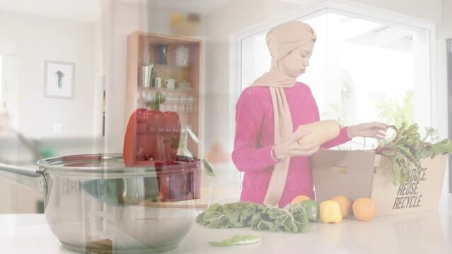 Biracial woman in hijab taking vegetables out of box in kitchen over pepper falling into pot