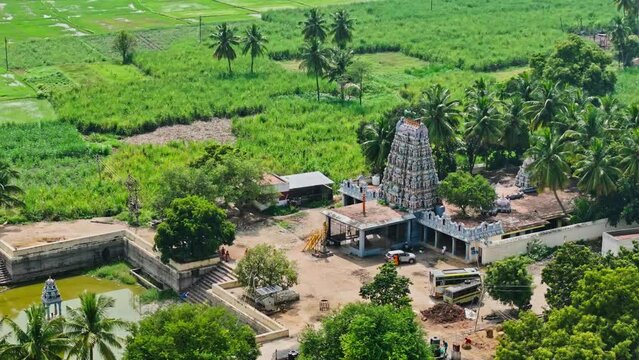 Rotating aerial side view of vintage Theni Temple with a pond in front and trees and greenery at background during sunny day in Theni, Tamil Nadu.