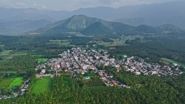 Profile view of a crowded city with trees and hills during a foggy cloudy day in Theni, Tamil Nadu. Aerial Shot.