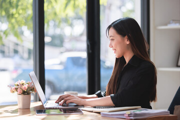 A successful businesswoman, seated at her office desk, works diligently on her laptop, showcasing professionalism and confidence in a corporate setting