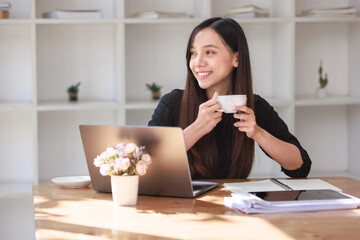 Smiling businesswoman happily working on her laptop at home, enjoying a cup of coffee in the kitchen