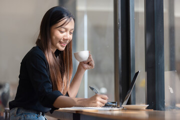 Smiling businesswoman in a suit working on her laptop and enjoying a cup of coffee at her office desk