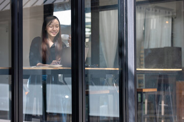 Businesswoman with a warm smile standing near an office window, looking out with elegance and style