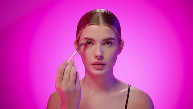 Attractive young nordic woman applies makeup powder on her eyes, close up shot in studio