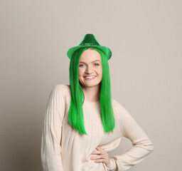St. Patrick's day party. Pretty woman with green hair and leprechaun hat on grey background