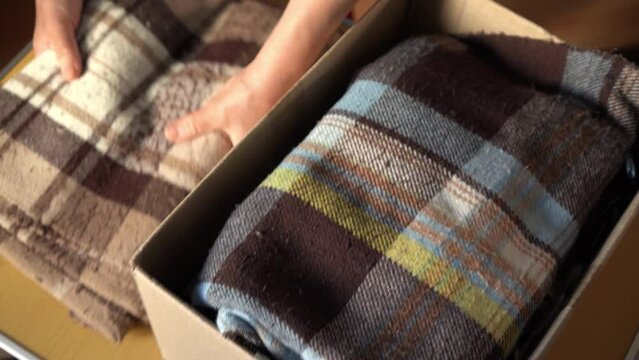 Volunteer stacking warm plaid blankets in a donation box. Donate. moving. Woman folding clothes, close up	