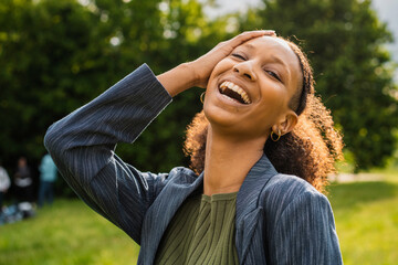 Young African woman laughing with hand on head in a park, radiating joy and vivacity.