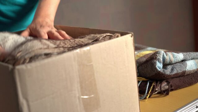 Volunteer stacking warm plaid blankets in a donation box. Donate. moving. Woman folding clothes, close up	