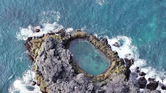 Aerial drone summer view with an azimuthal backward movement, close-up of the rocky Brimketill Pool with waves in the Reykjanes Peninsula, Iceland.