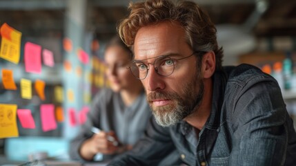 Obraz premium A focused man with glasses in front of colorful sticky notes on a wall, another person blurred., generative ai