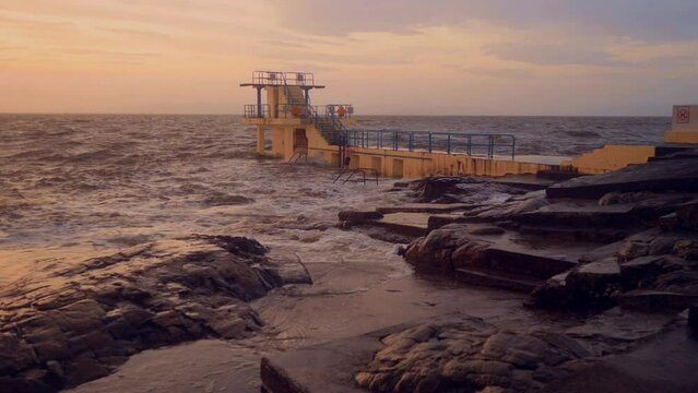 Blackrock diving board hit by ocean waves at sunrise. Popular city landmark in Galway city, Ireland. Famous tourist area in Salthill. Water motion and stone coastline. Warm tone.