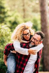 Happy adult caucasian couple in relationship and love play together in the forest wood nature - outdoor people leisure activity concept with cheerful caucasians