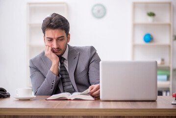 Young male employee reading book in the office