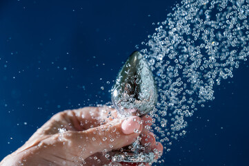 Woman washing silver butt plug under shower on blue background. 