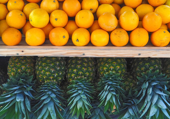 Group of whole ripe pineapples and oranges on a wooden shelf