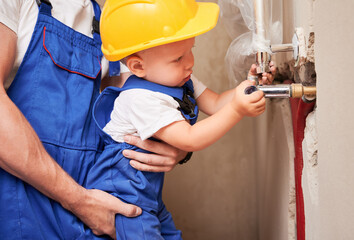 Close up of male plumber holding little boy while child installing plumbing pipes in apartment...