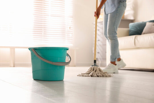Plastic bucket and woman mopping floor in living room, closeup. Cleaning supplies