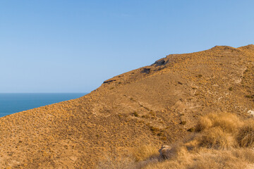 Colinas costeras al norte de Las Negras, Almería, España. Empinadas cuestas rocosas cubiertas de pasto seco en verano junto al mar Mediterráneo. Parque Natural del Cabo de Gata.