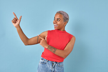 Young cheerful beautiful African American woman points fingers to side and laughs offering to place...