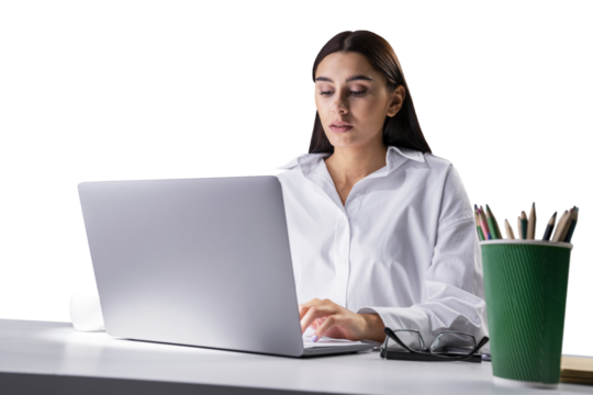 Serious businesswoman focused on laptop work, white shirt and office backdrop