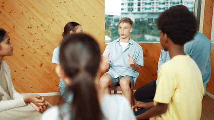 Attractive boy sharing experience during attend in group therapy. Highschool student talking about way to recovery stress while surrounded with multicultural friend listeing carefully. Edification.