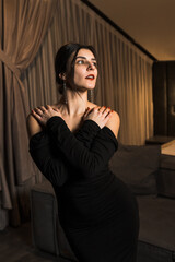 Elegant woman in a black dress posing in an apartment. Fashion shooting concept