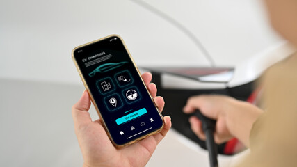 Man using EV application on his phone to check charging status while plugged in the EV charging connector