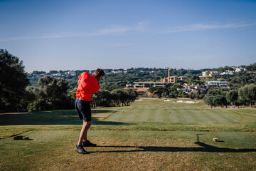 Sotogrante, Spain - January 27, 2024 - Man in red shirt and black shorts preparing to swing a golf...