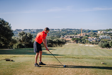 Sotogrante, Spain - January 27, 2024 - Man in red shirt and black shorts preparing to swing a golf...