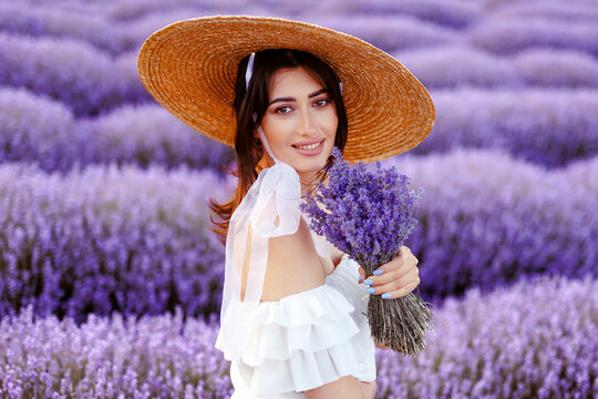 ,beautiful woman portrait in lavender field in white dress and straw hat holding a bouquet of lavender flowers