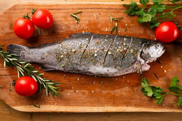 Fresh river trout with tomatoes and herbs de Provence on a kitchen wooden board. Cooking delicious and healthy food at home.Fresh fish trout and ingredients for cooking. Raw fish.