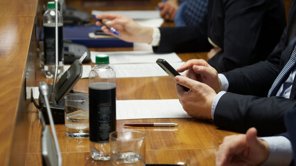 Man uses a cell phone, a smartphone, while sitting with colleagues at a table. Business meeting, meeting or negotiation. Politician, official or manager. Without a face. Photo - obrazy, fototapety, plakaty