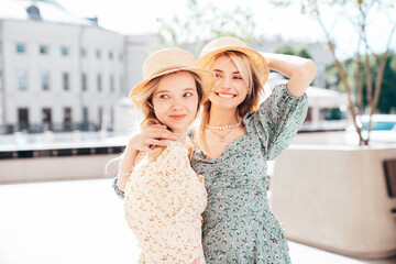 Two young beautiful smiling hipster female in trendy summer dress  clothes. Blond carefree women posing in the street. Positive models having fun at sunny day. Going crazy. In sundress