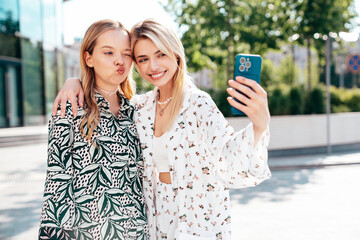 Two young beautiful smiling hipster female in trendy summer costumes  clothes. Sexy carefree women posing in the street. Positive models having fun at sunny day. Going crazy