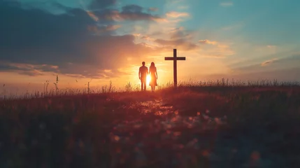 Fotobehang Couple praying together in field in front of cross at sunset © IBEX.Media