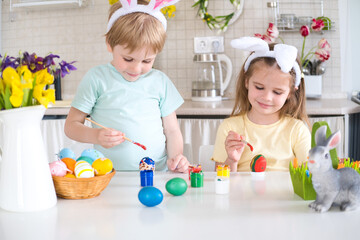 Happy kids painting easter eggs in kitchen 